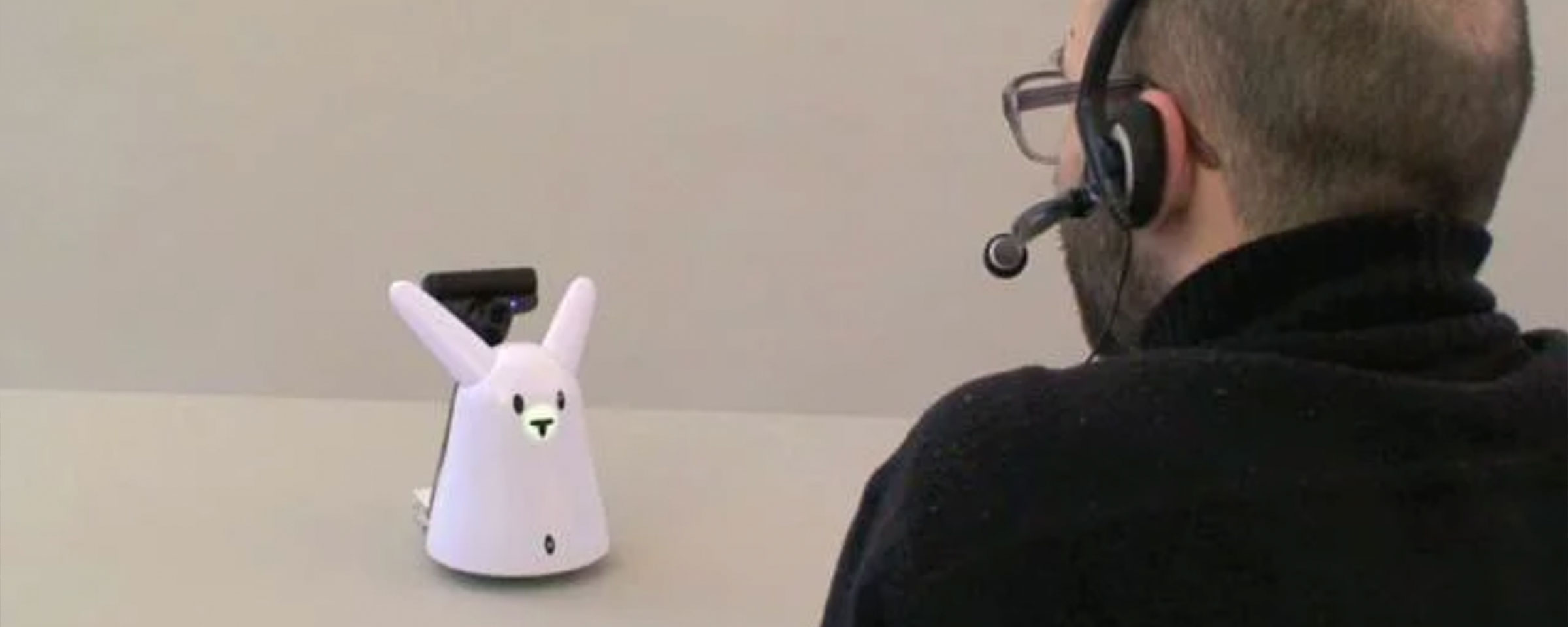 Benedikt Groß talks by headset with a robot which has the shape of a rabbit