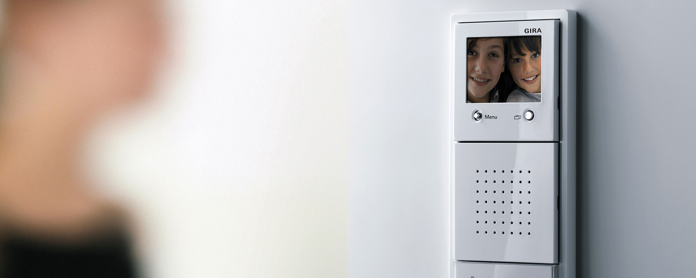 White door communication system, with a person in front of it, displays children on a monitor